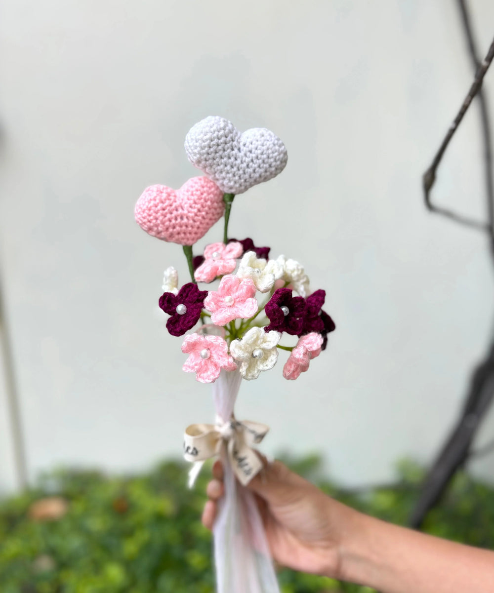 Hand holding crochet flower bouquet with pink, white hearts and ribbon bow outdoors