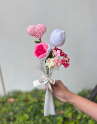 Hand holding a bouquet of crocheted flowers and heart with pastel colors, gift ready