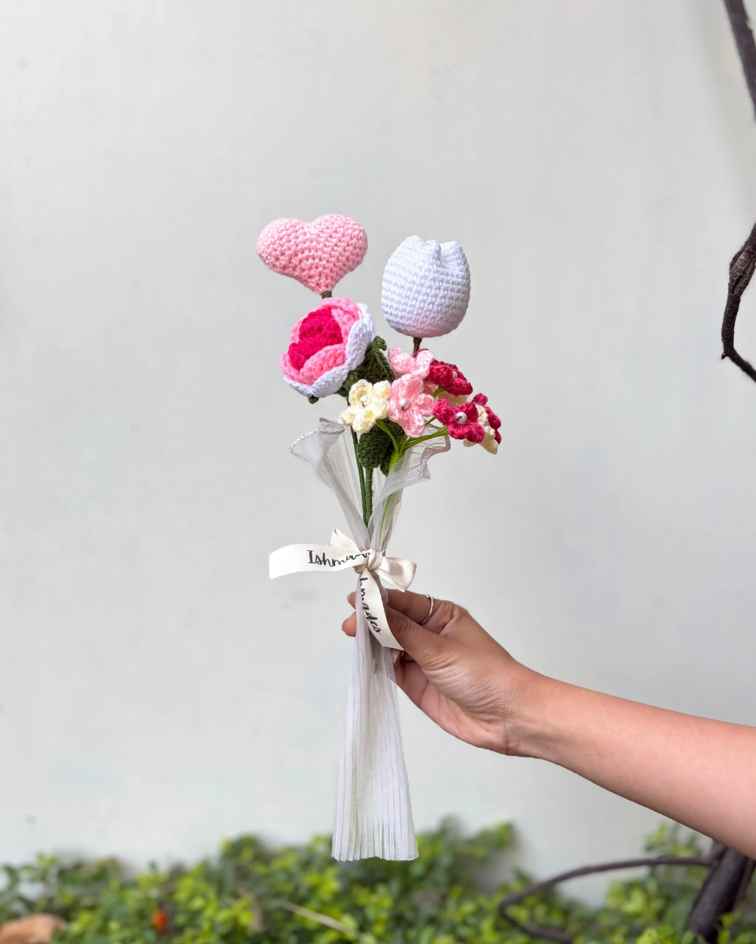 Hand holding a bouquet of crochet flowers and heart with ribbon, gift arrangement